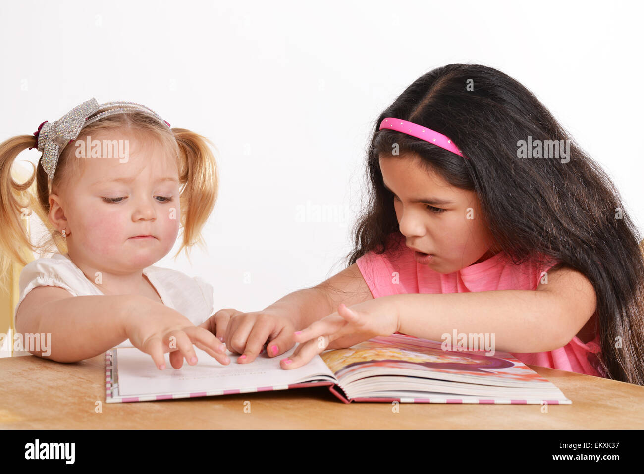 Two young girls reading a book at home Stock Photo