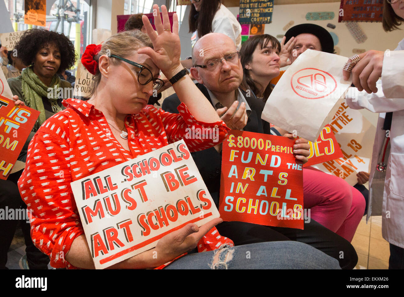 London, UK. 13 April 2015. Artist Bob and Roberta Smith (orange T-shirt) poses with BA and MA fine art students, alumni and lecturers of The Cass, London Metropolitan University who dish out medicine against funding cuts. Over three weeks leading up to the General Election when artist Bob and Roberta Smith (Patrick Brill) will stand against Michael Gove in the Surrey Heath constituency, Smith/Brill will lead students and activists at The Arts Emergency Response Centre at the Cass Bank Gallery in an indoor protest against art funding cuts. Photo: Bettina Strenske Stock Photo