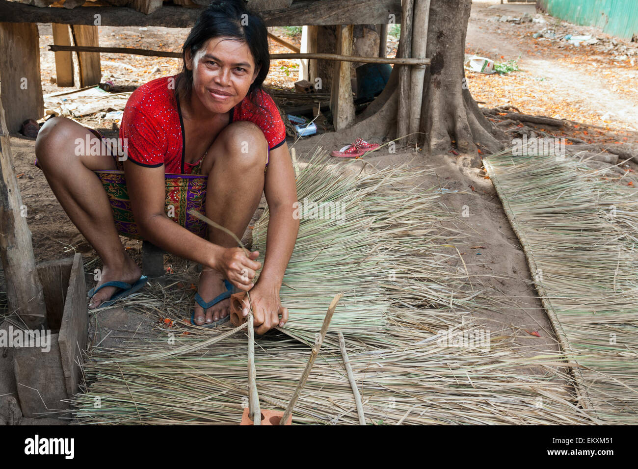 Cambodian woman weaving palm fronds to make a house roof in Kep