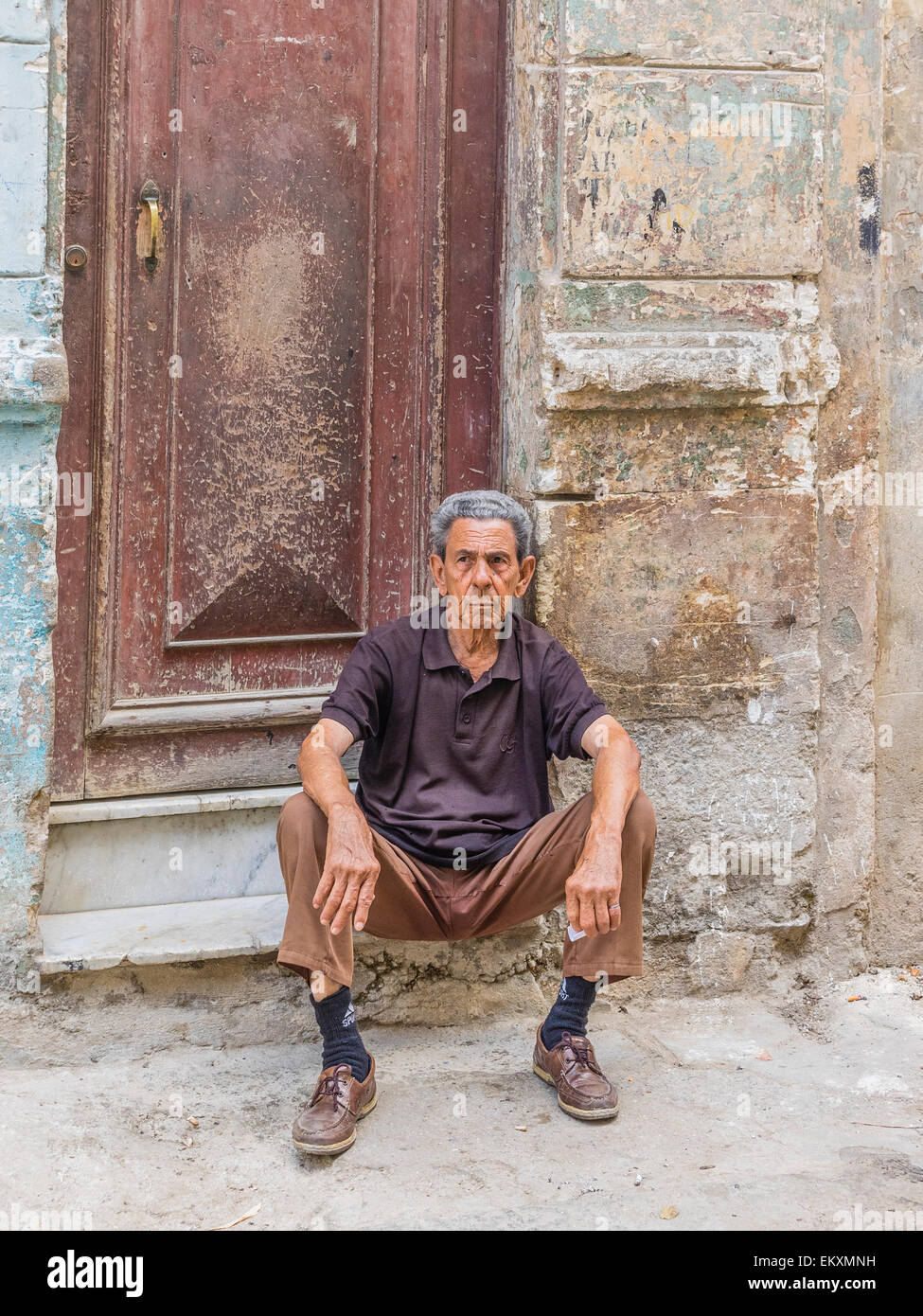 A Cuban Hispanic man sits on the stoop in front of his house with crumbling wall in Havana Vieja, Cuba. Stock Photo
