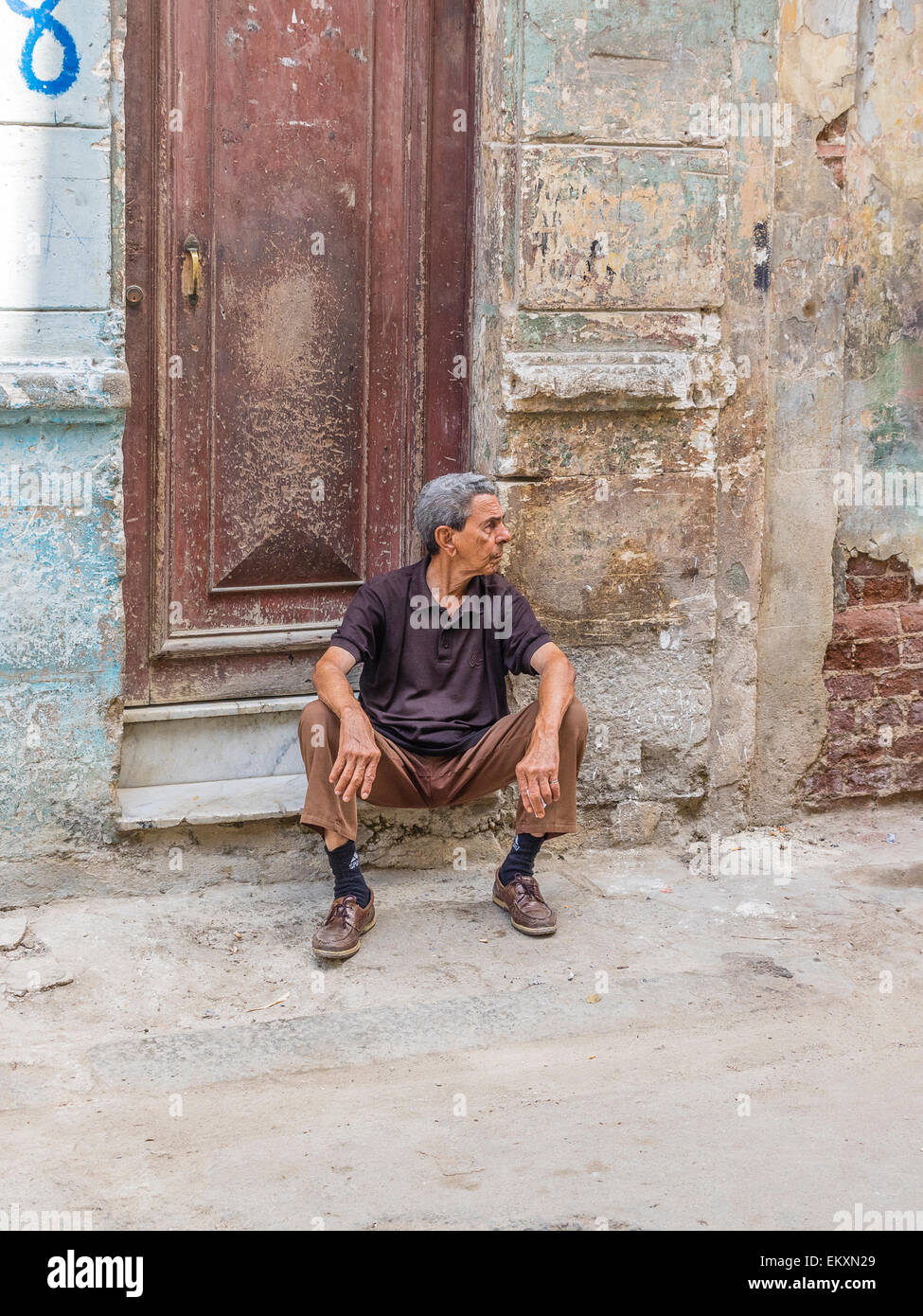 A Cuban Hispanic man sits on the stoop in front of his house with crumbling wall in Havana Vieja, Cuba. Stock Photo