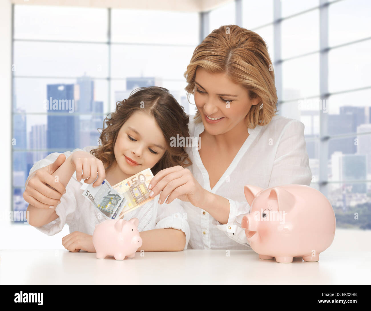 mother and daughter putting money to piggy banks Stock Photo - Alamy