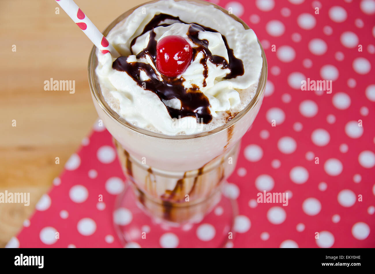 Ice cream sundae with drizzled chocolate and maraschino cheery and polka dot straw. Stock Photo