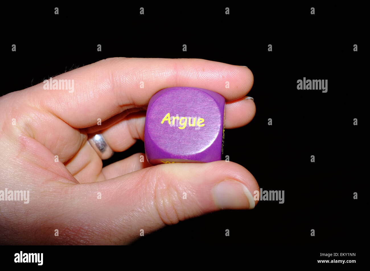 A white hand holding a purple activity dice against a black background Stock Photo