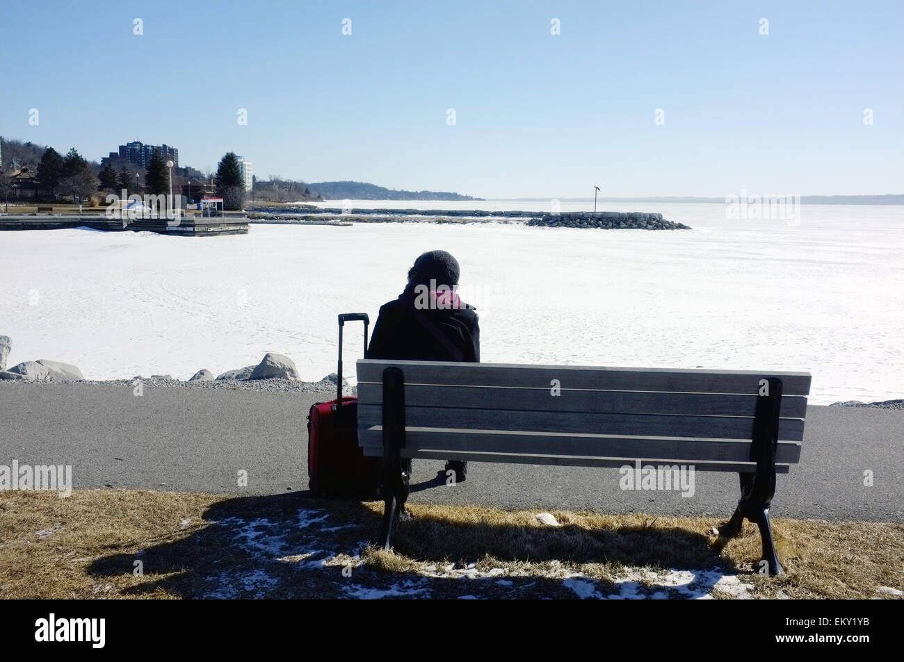 A woman sits on a bench overlooking the frozen lake Simcoe on the edge of Barrie in Canada. Stock Photo