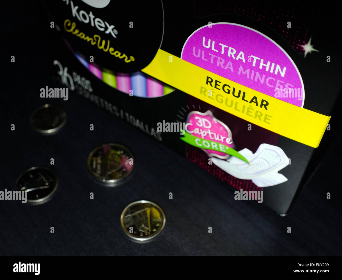 A packet of thin sanitary pads with coins photographed against a black background. Stock Photo