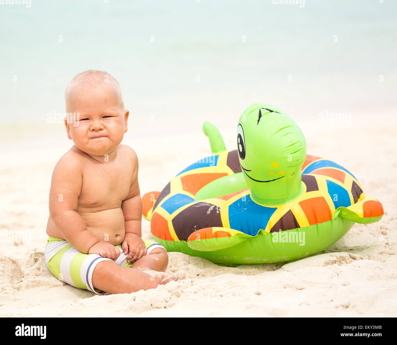 Baby sitting om the beach with swim ring Stock Photo