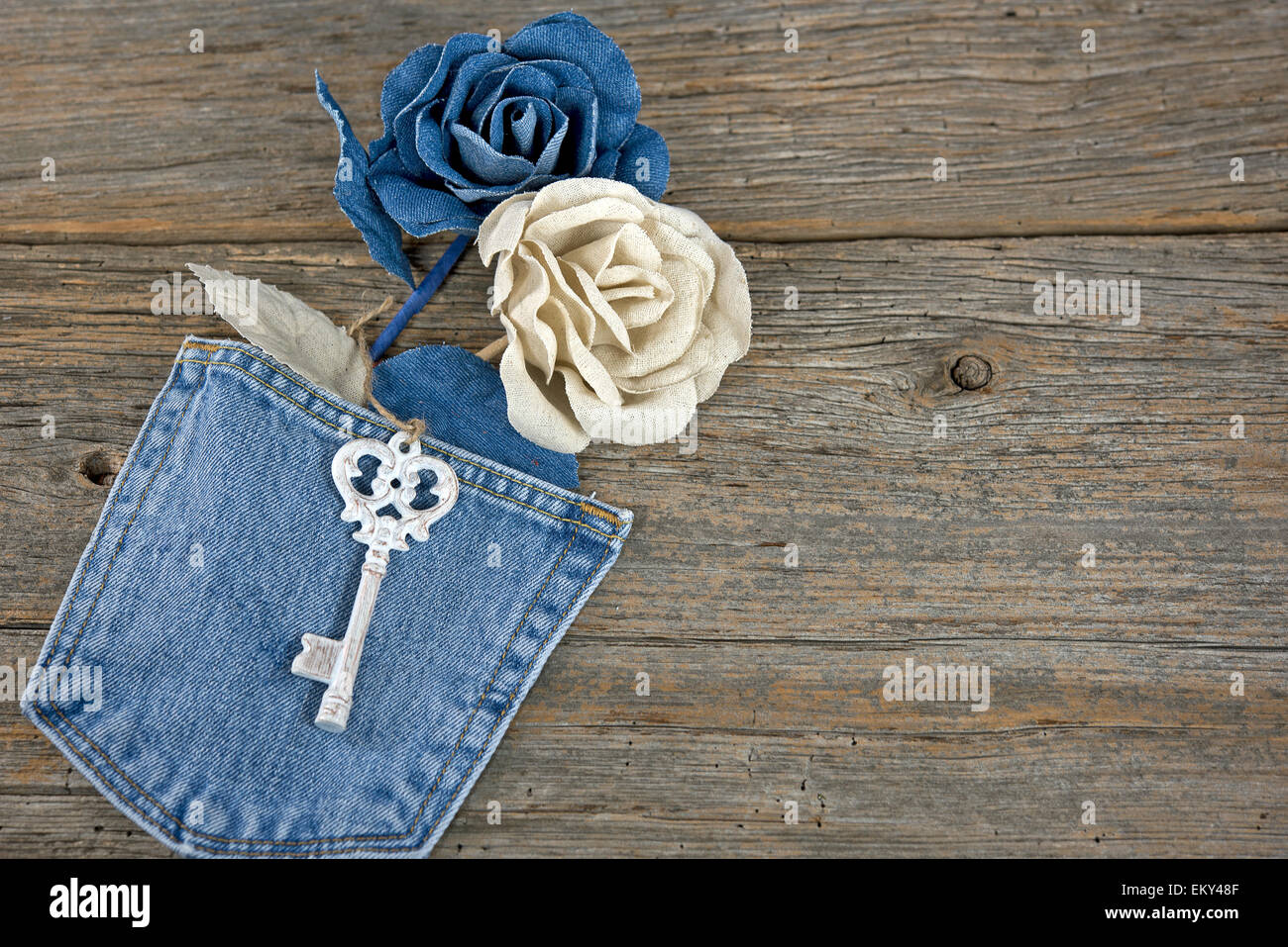 Denim roses in blue jean pocket with antique key on rustic wood. Stock Photo