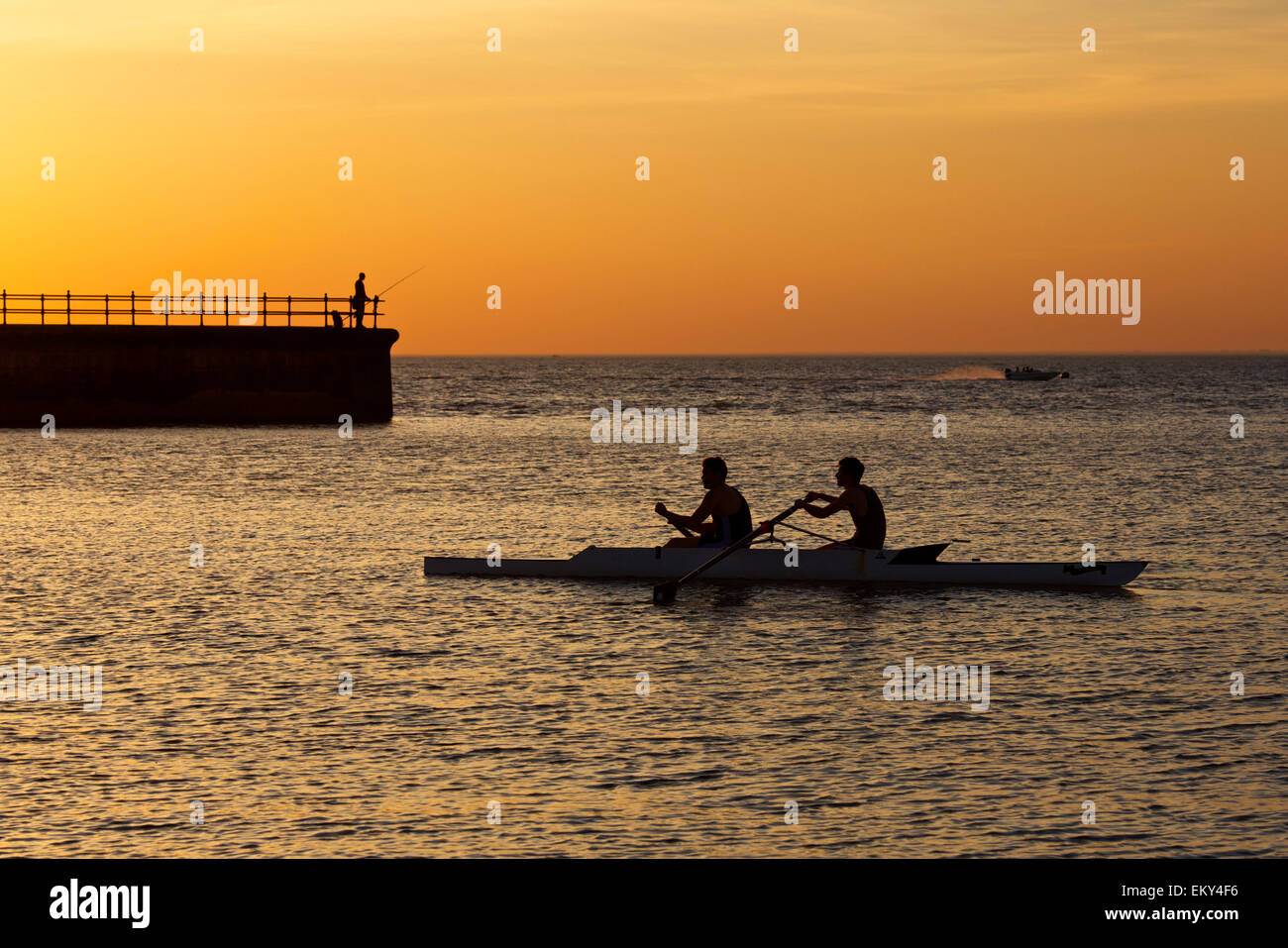 Hampton, Kent, UK. 14th April 2015: UK Weather. Sunset at Hampton near Herne Bay in Kent as an angler fishes from the pier, rowers and a speedboat are making the most of the last rays of light after a glorious hot day with more good weather forecast for Wednesday Stock Photo