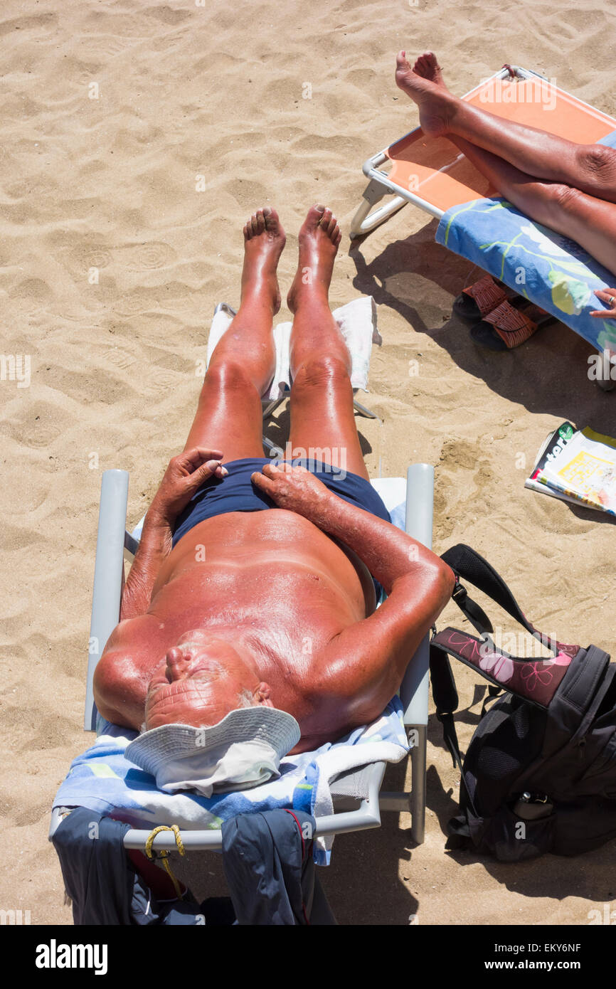 Elderly couple with deep tans sunbathing on beach in Spain Stock Photo