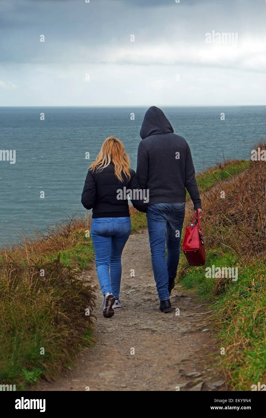 Foreign Polish Migrant couple walk hand in hand on the cliff walk around Howth Head in changeable weather on the coast in North Dublin Ireland Stock Photo