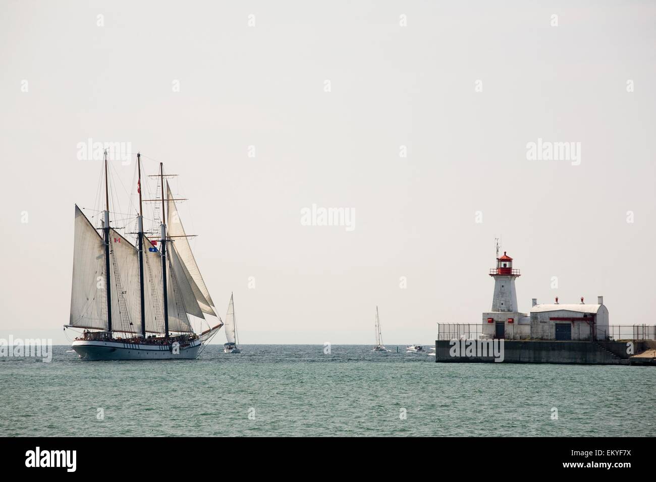 Tall Ship With Sails And A Lighthouse; Port Colborne, Ontario, Canada Stock Photo