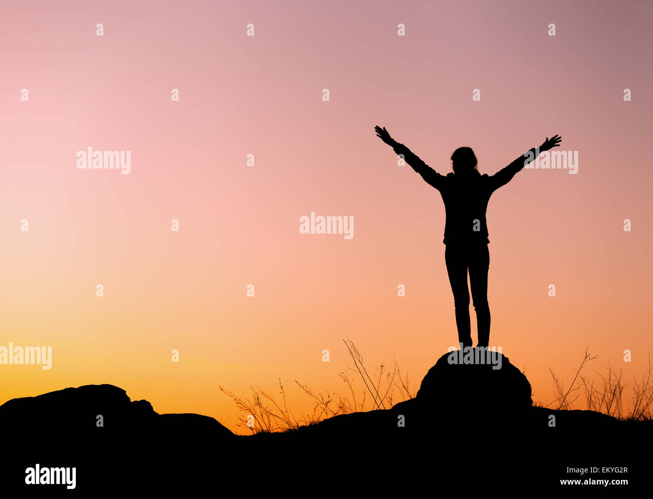 Silhouette of happy young woman with arms raised up against beautiful colorful sky. Summer Sunset. Landscape Stock Photo