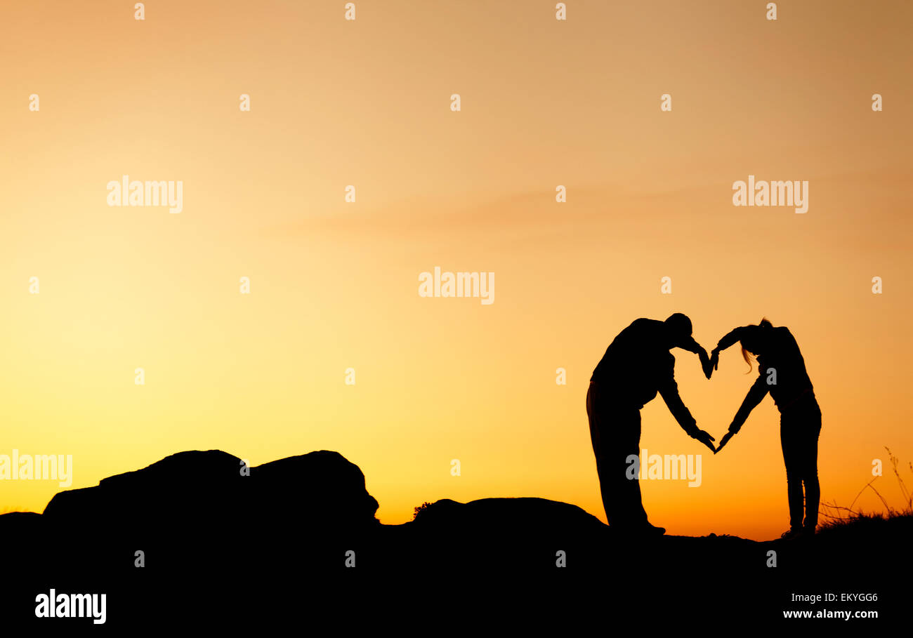 Conceptual heart shape, symbol of human. Woman and man hand silhouette over sky at sunset background, metaphor to love Stock Photo