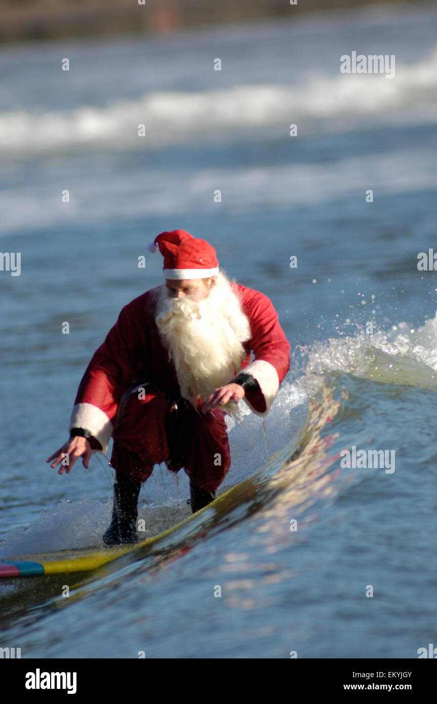 Santa Claus goes surfing and catches a wave on a yellow surf board Stock Photo
