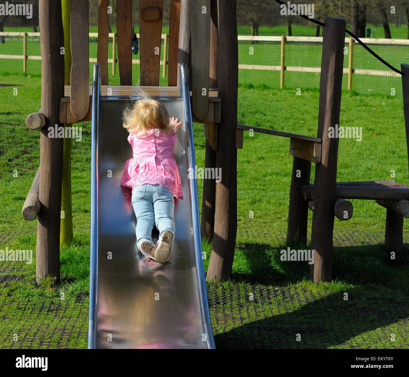 A 2 year old toddler girl coming backwards down a park slide England,UK Stock Photo