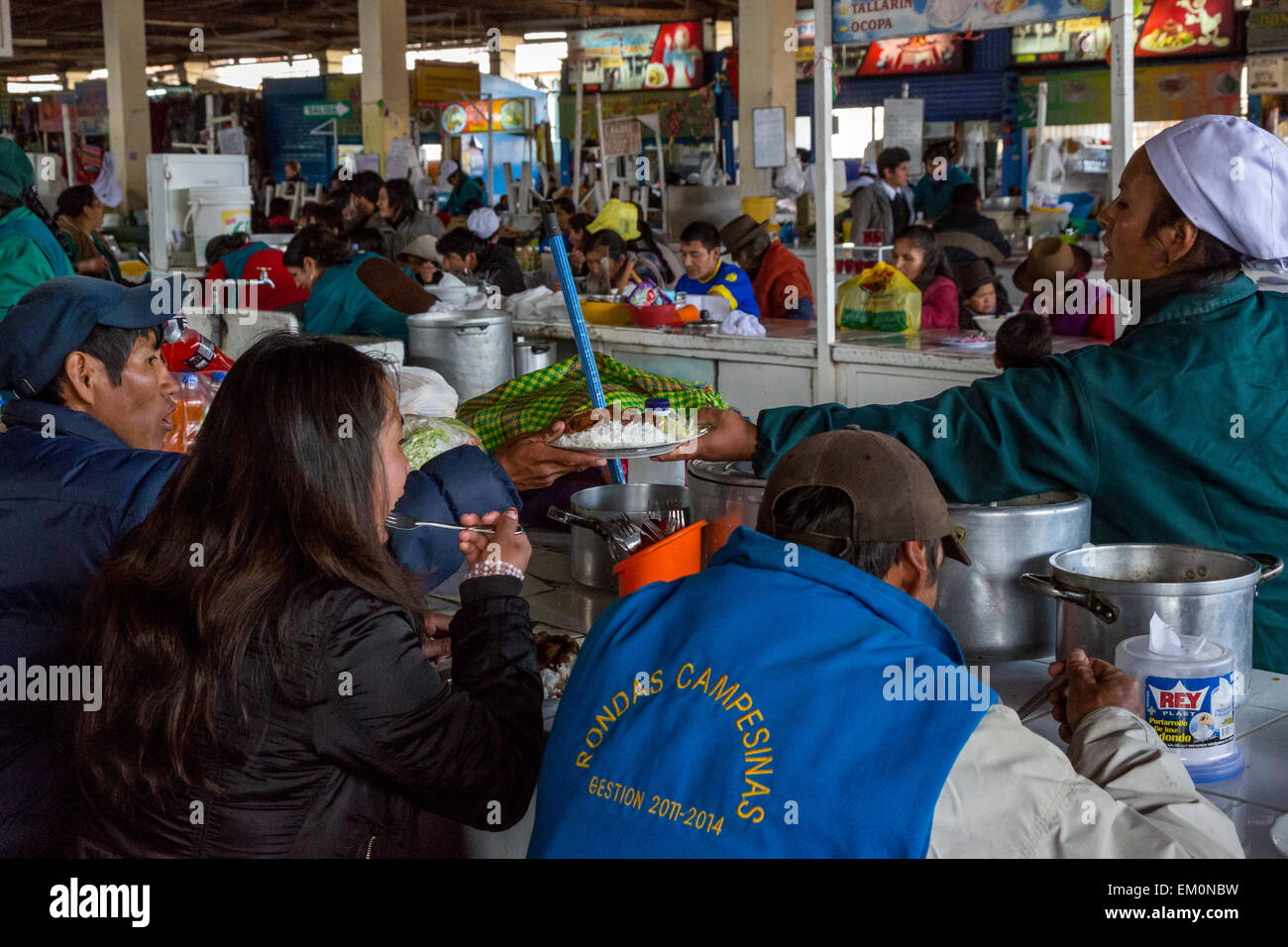 Peru, Cusco, San Pedro Market.  Cook Passing Lunch to a Customer Eating in the Food Court Area of the Market. Stock Photo