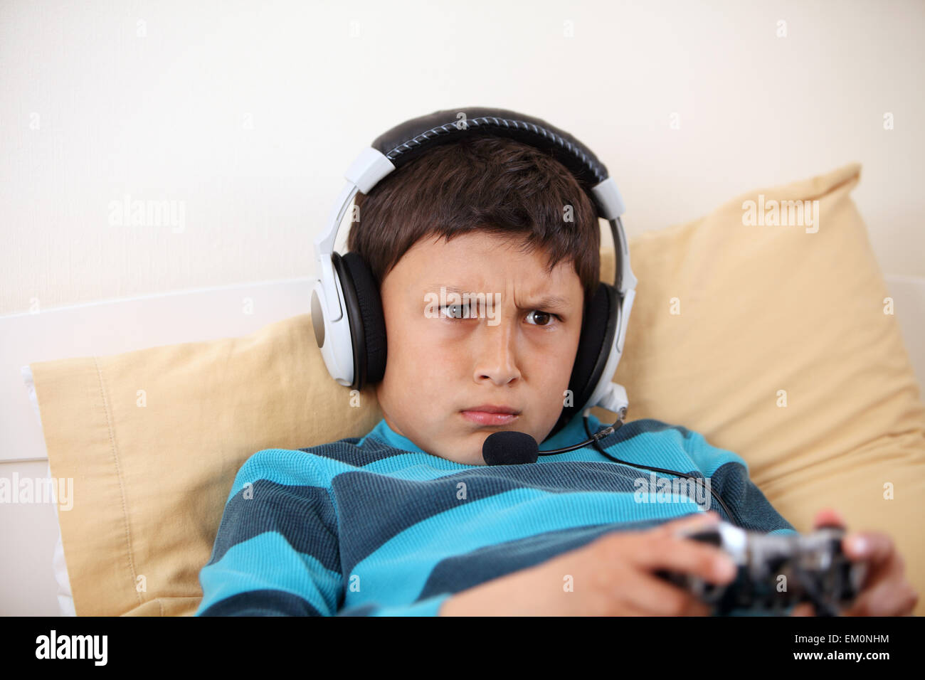 Young boy frowns while playing video game with his friends with headset and microphone with copy space Stock Photo