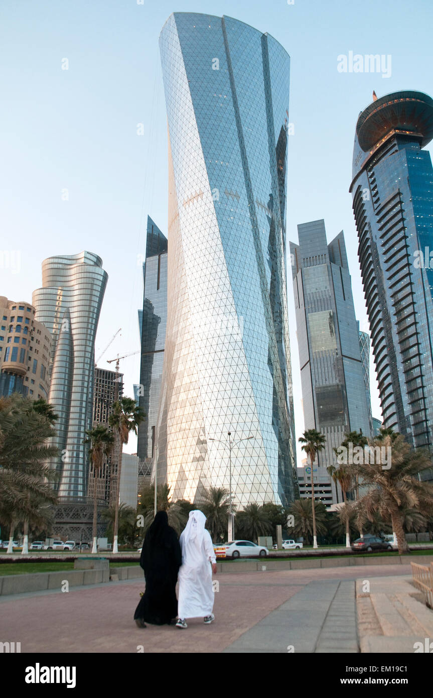 A man and woman in traditional clothes walk below skyscrapers in the city of Doha, Qatar. Stock Photo