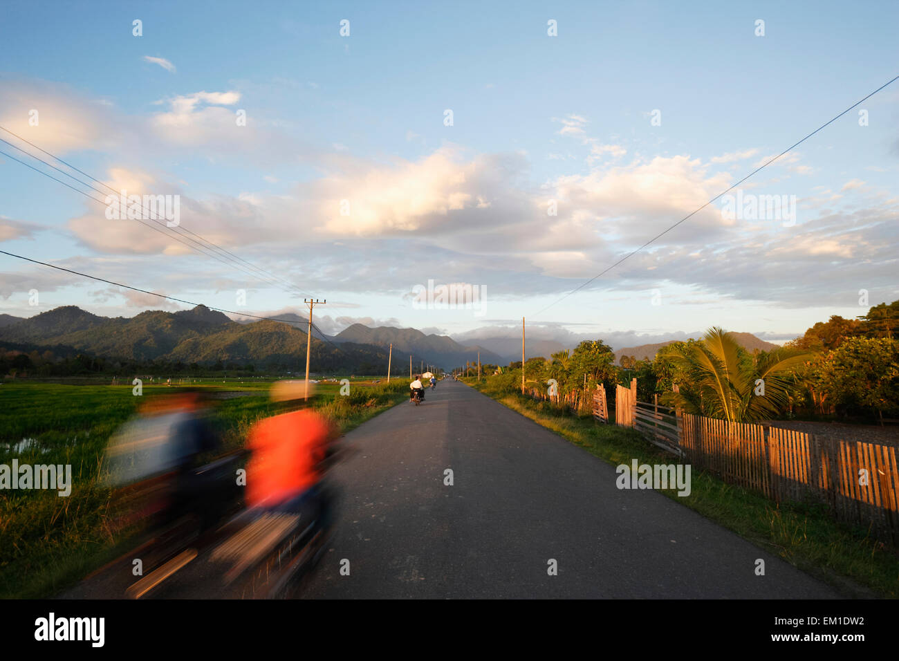 Cyclists speed along the road; Lamno, Aceh Province, Sumatra, Indonesia Stock Photo