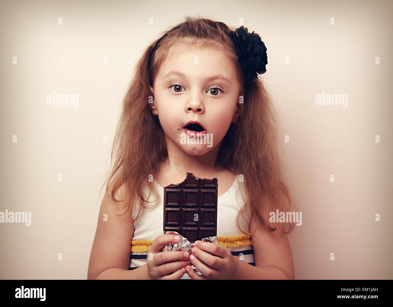 Surprising kid girl looking with big eyes and holding chocolate. Vintage portrait Stock Photo