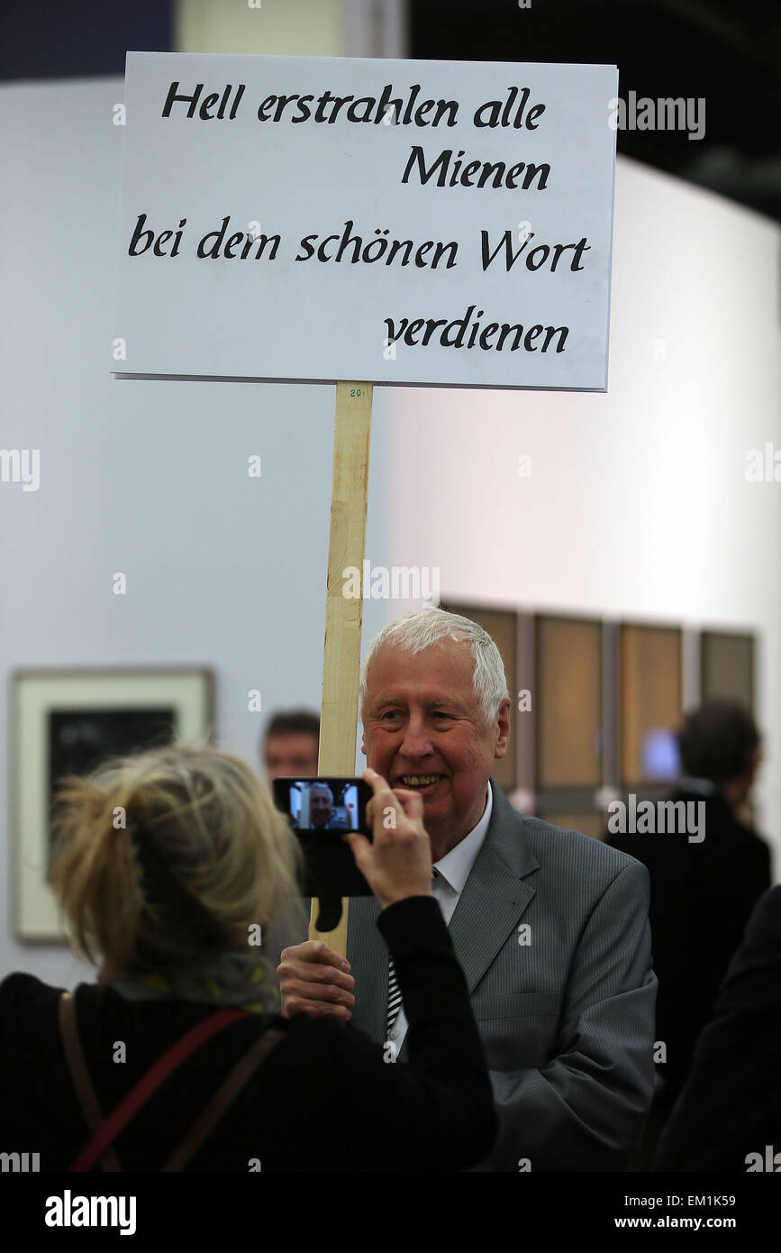 Cologne, Germany. 15th Apr, 2015. A 74-year old man protests with a sign reading 'Hell erstrahlen alle Mienen bei dem schönen Wort verdienen' (Everyone's faces are lighted up when they hear the word earn) at the art fair Art Cologne in Cologne, Germany, 15 April 2015. The fair runs from 16 until 19 April 2015. Photo: OLIVER BERG/dpa/Alamy Live News Stock Photo