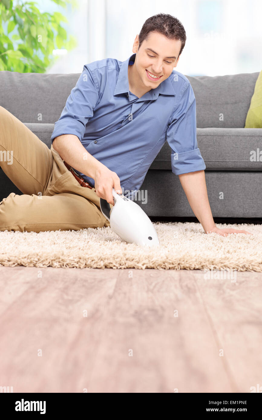 Vertical shot of a young man holding a handheld vacuum cleaner and