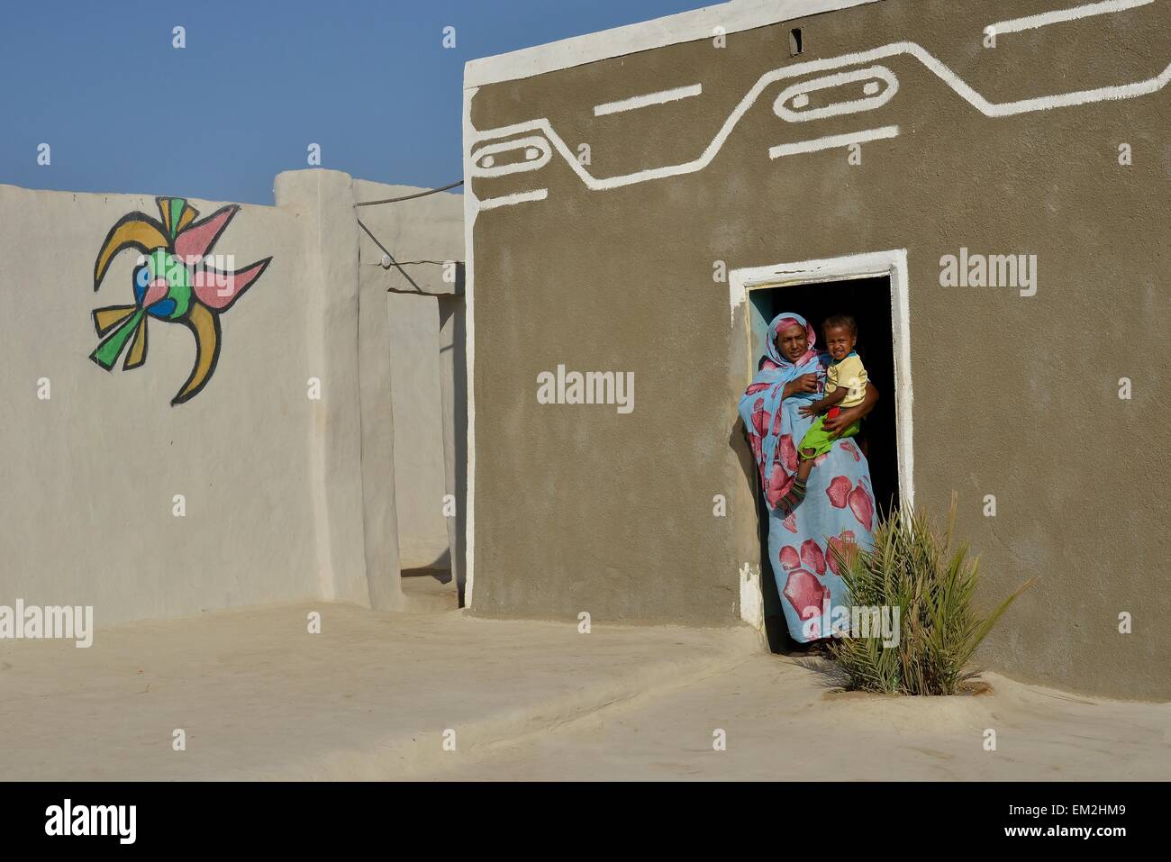 Woman carrying toddler, colorful painted Nubian house in the village Umogaal in Dongola, Nubia, Sudan Stock Photo