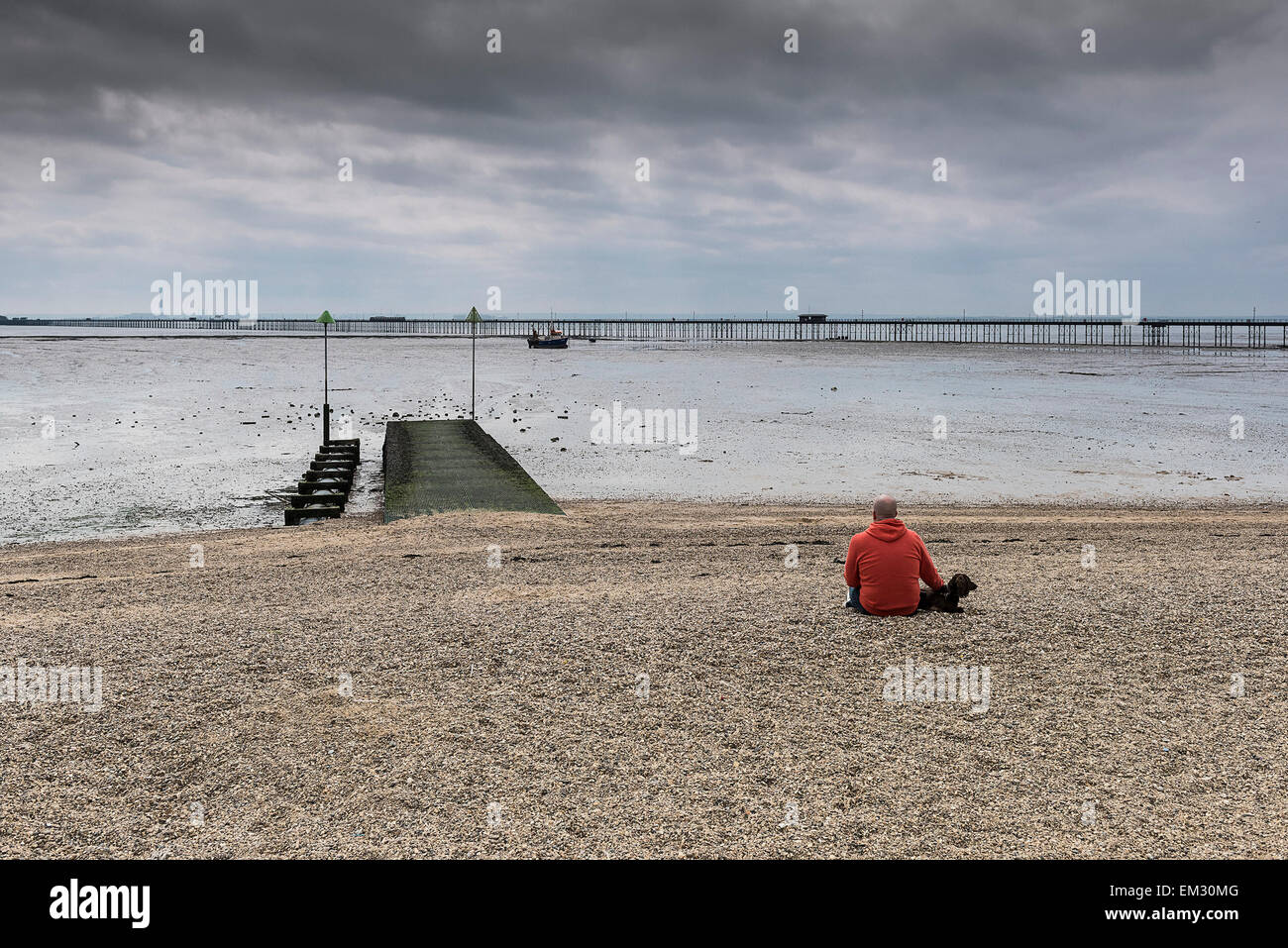 A man and his dog sitting on City Beach in Southend on a cloudy day. Stock Photo