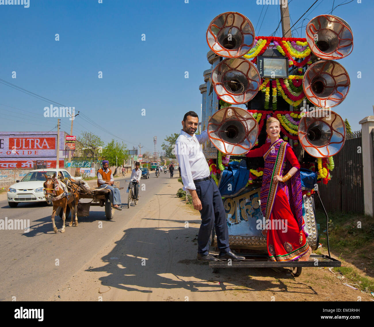 A Mixed Race Couple Stands On The Back Of A Decorated Cart On The Side Of The Road; Ludhiana, Punjab, India Stock Photo