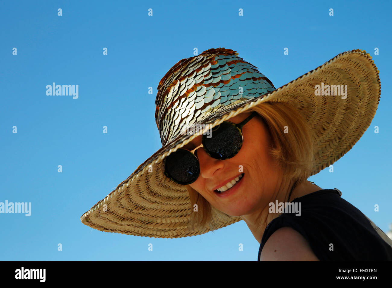 Sunbather Debbie Stokes protects her head with a gold sequined hat in the sunshine at Brighton in East Sussex April 15, 2015. Stock Photo