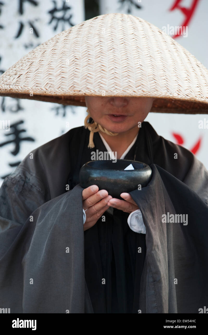 Japan, Kyoto, Woman wearing conical hat and black robe and holding bowl Stock Photo