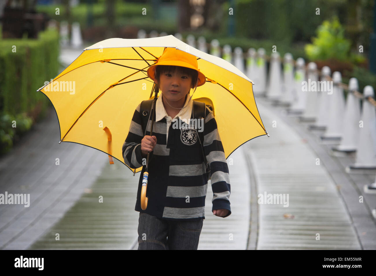 Japan, Tokyo, Girl walking in rain wearing yellow hat and holding yellow umbrella Stock Photo