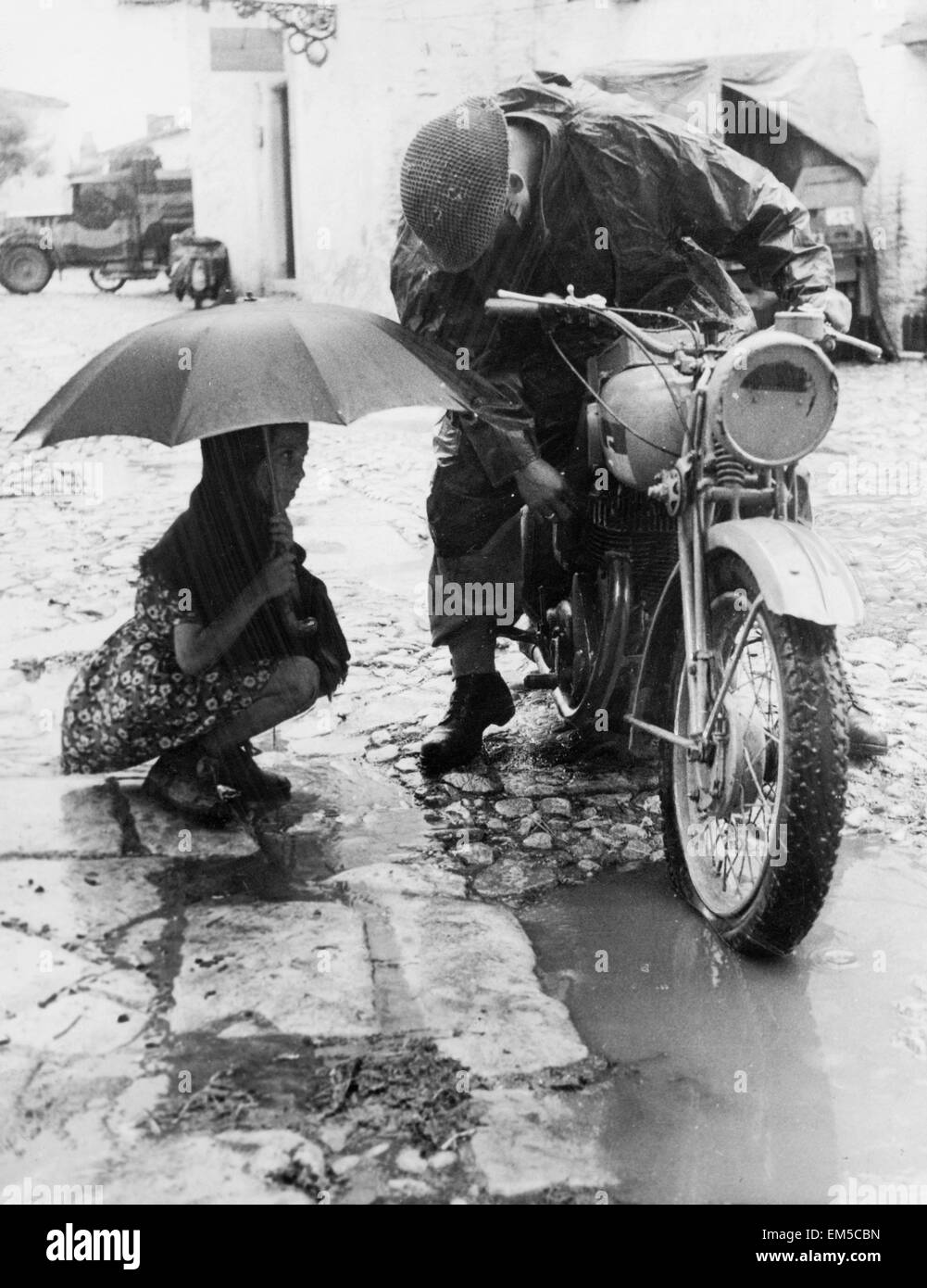 Heavy rains have added to the difficulties facing the 5th and 8th armies in Italy, October 1943. Pictured: dispatch rider forced to a halt, with water in his carburettor, as italian girl looks on with interest. Stock Photo