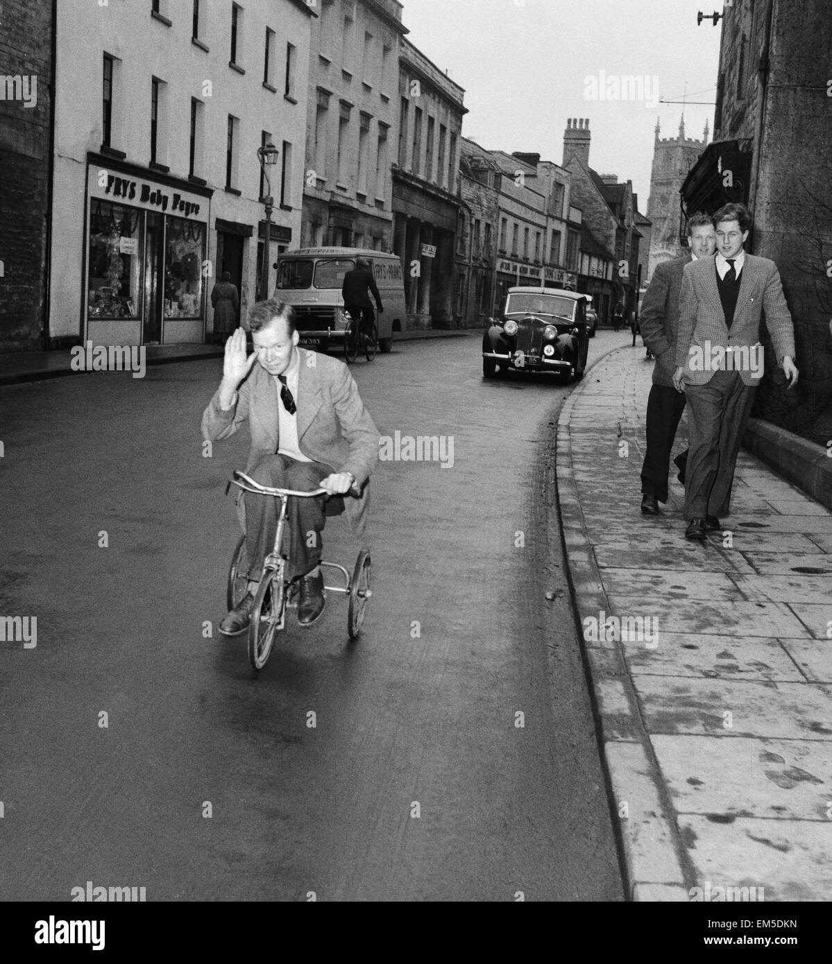 The Earl of Guilford rides through the town of Cirencester on a child's tricyle to win a £6 bet he made with a land owner's son. 6th December 1955. Stock Photo