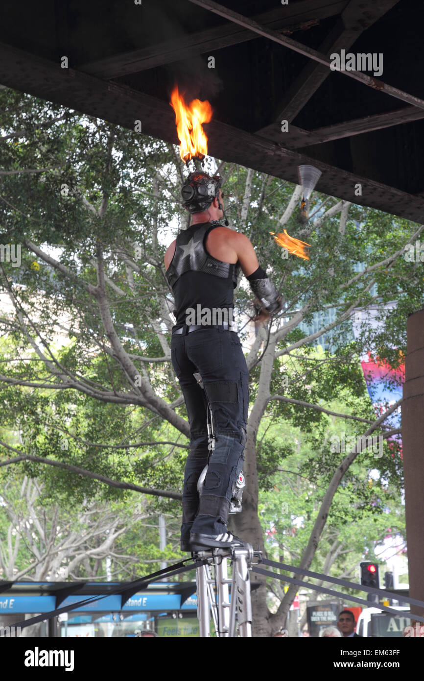 Street Artist juggling with burning torches while standing on a stand during a performance at  Circular Quay, Sydney, Australia. Stock Photo