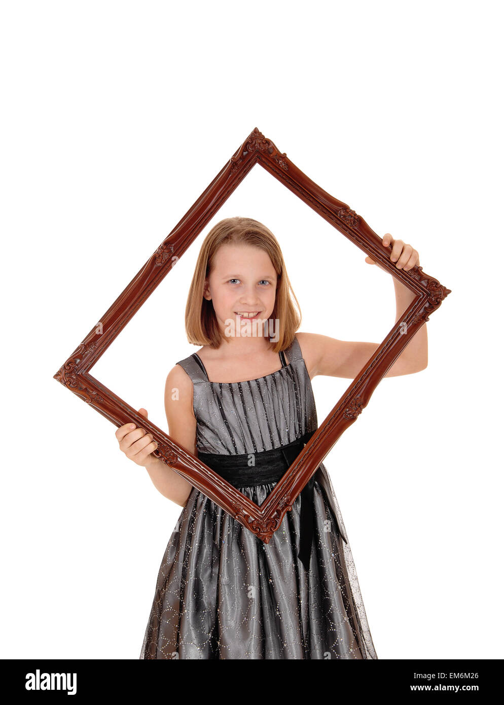 A lovely young girl in a grey dress holding a picture frame in front of her, isolated on white background. Stock Photo