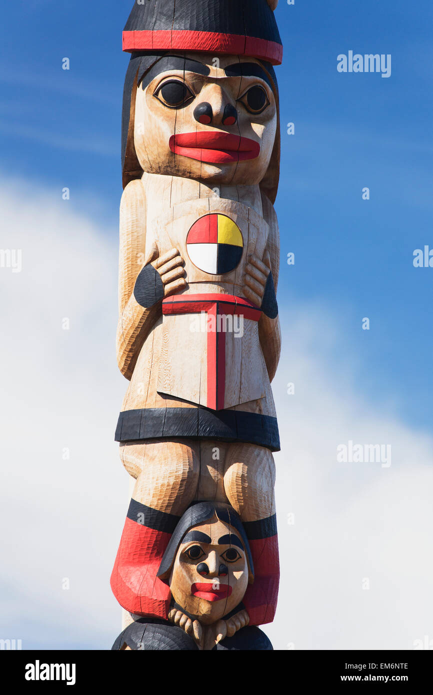 Human figures carved and painted on a wooden totem pole against a blue ...