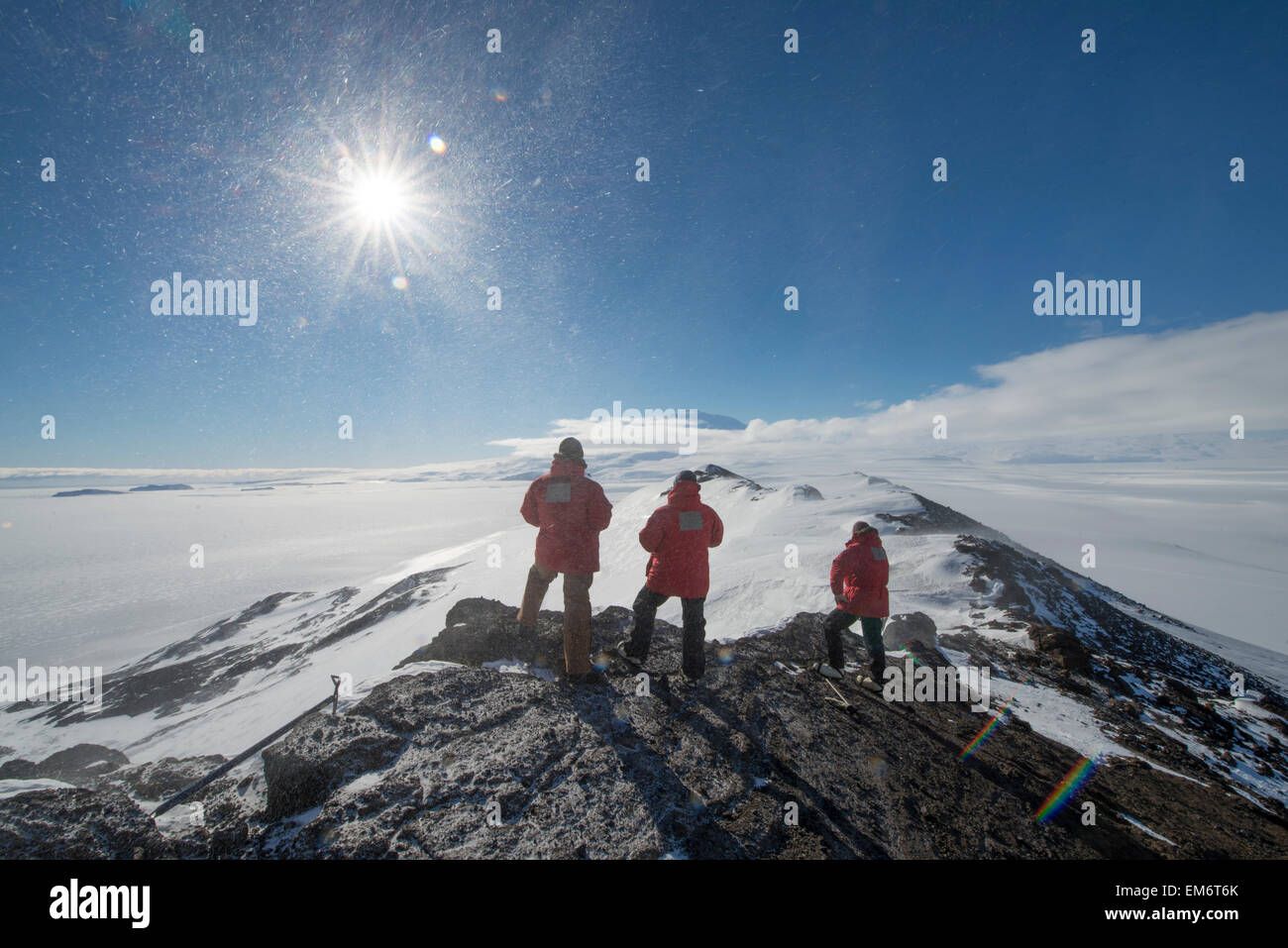 Three men overlook Erebus Bay from Castle Rock on Ross Island, Antarctica in high winds. Stock Photo