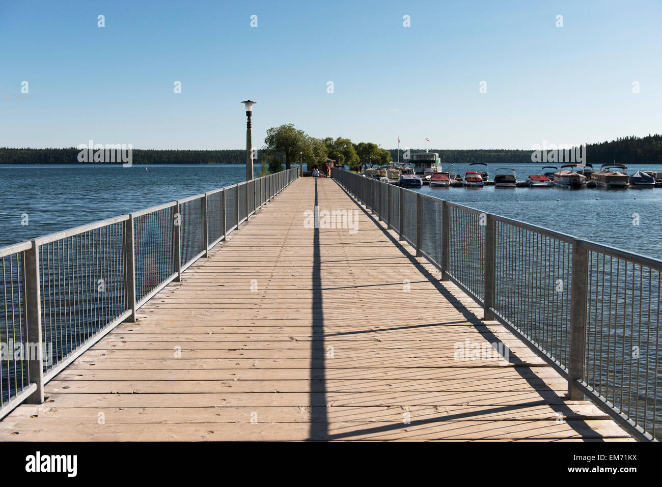 A wooden boardwalk leading out to the water and boats mooring in a harbour; Manitoba, Canada Stock Photo