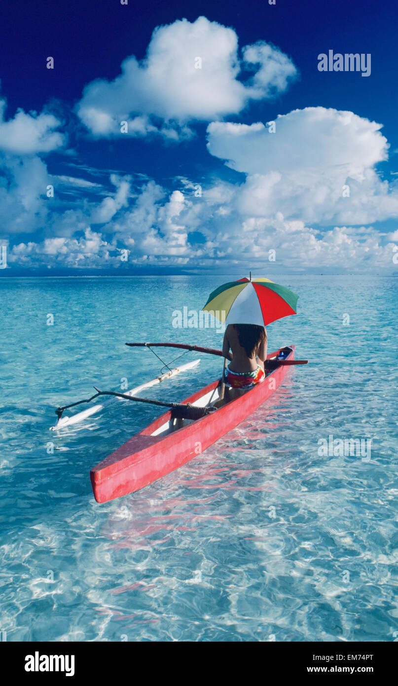 French Polynesia, Tetiaroa, Local Woman In Outrigger Canoe With Umbrella, View From Behind. Stock Photo