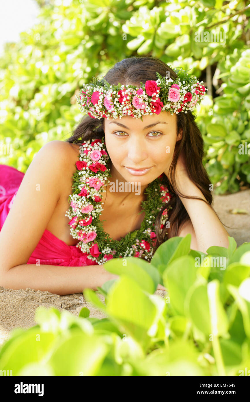 Hawaii, Local Girl Laying On Sand Wearing Flower Leis Surrounded By Bright Vegetation Stock