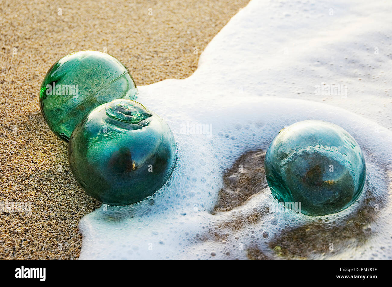 Three Glass Fishing Floats Roll On The Sandy Shoreline With