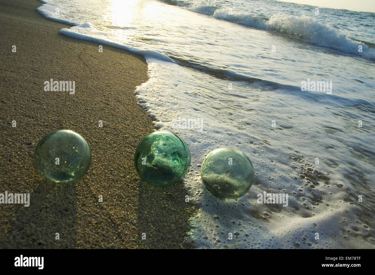 Three Glass Fishing Floats Roll On The Sandy Shoreline With Ripples Of