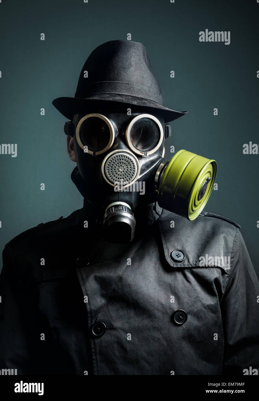 Man in gas mask, raincoat and black hat at dark background Stock Photo