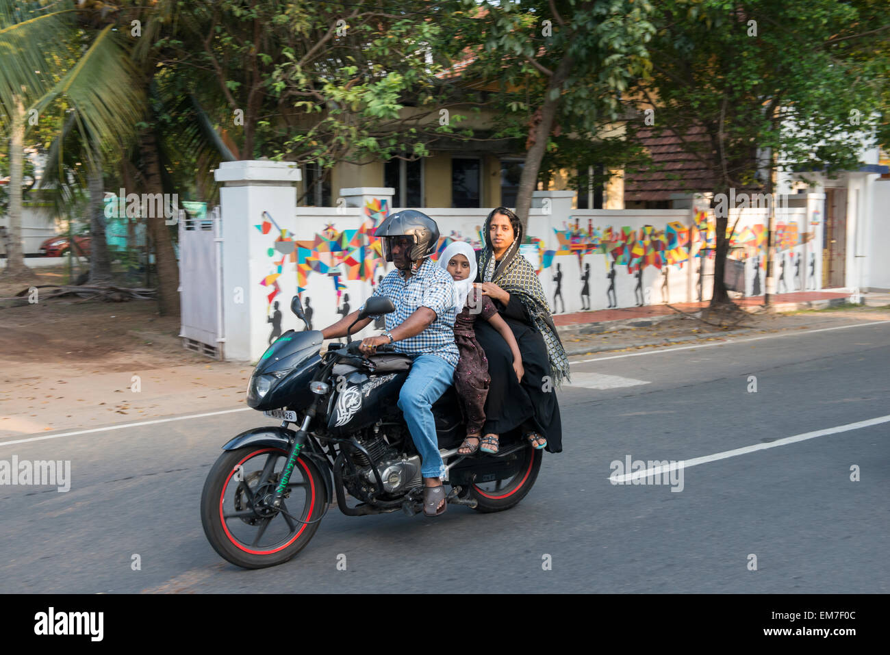 A young family riding a motorcyle through Fort Kochi, Kerala India Stock Photo