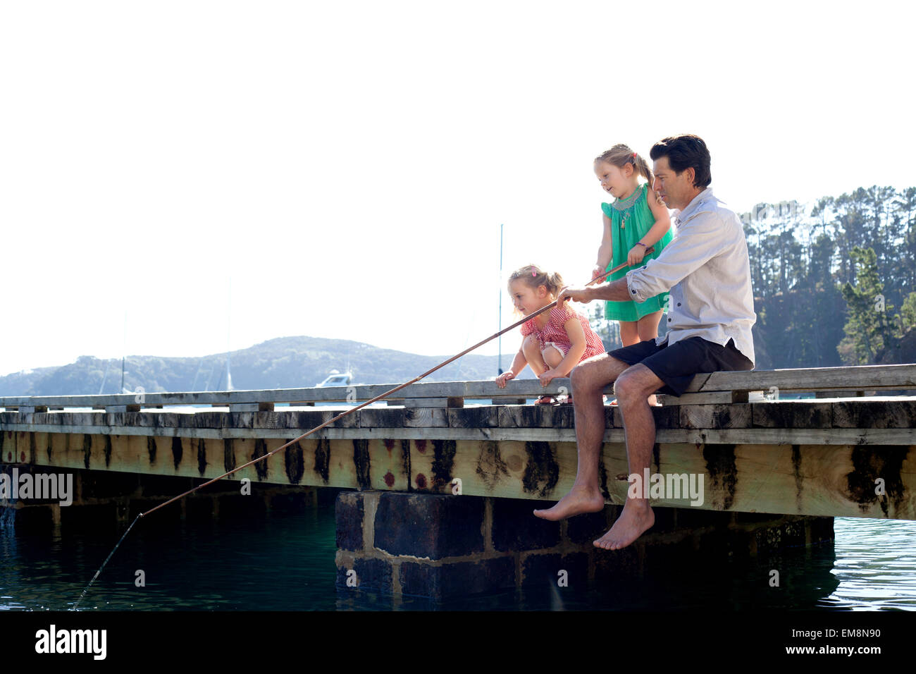 Mature man and daughter fishing from sea pier, New Zealand Stock Photo