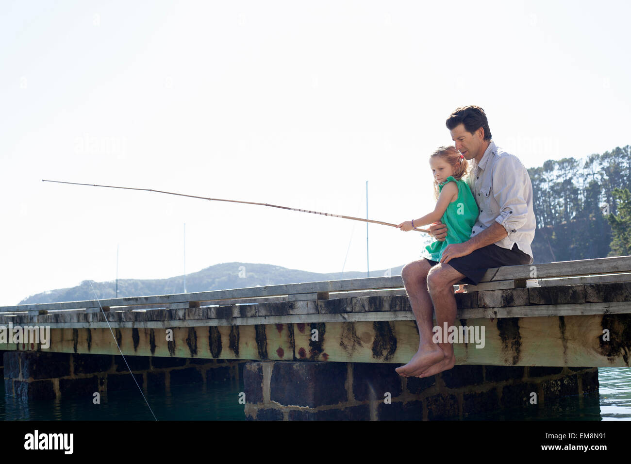 Mature man and daughter fishing on sea pier, New Zealand Stock Photo