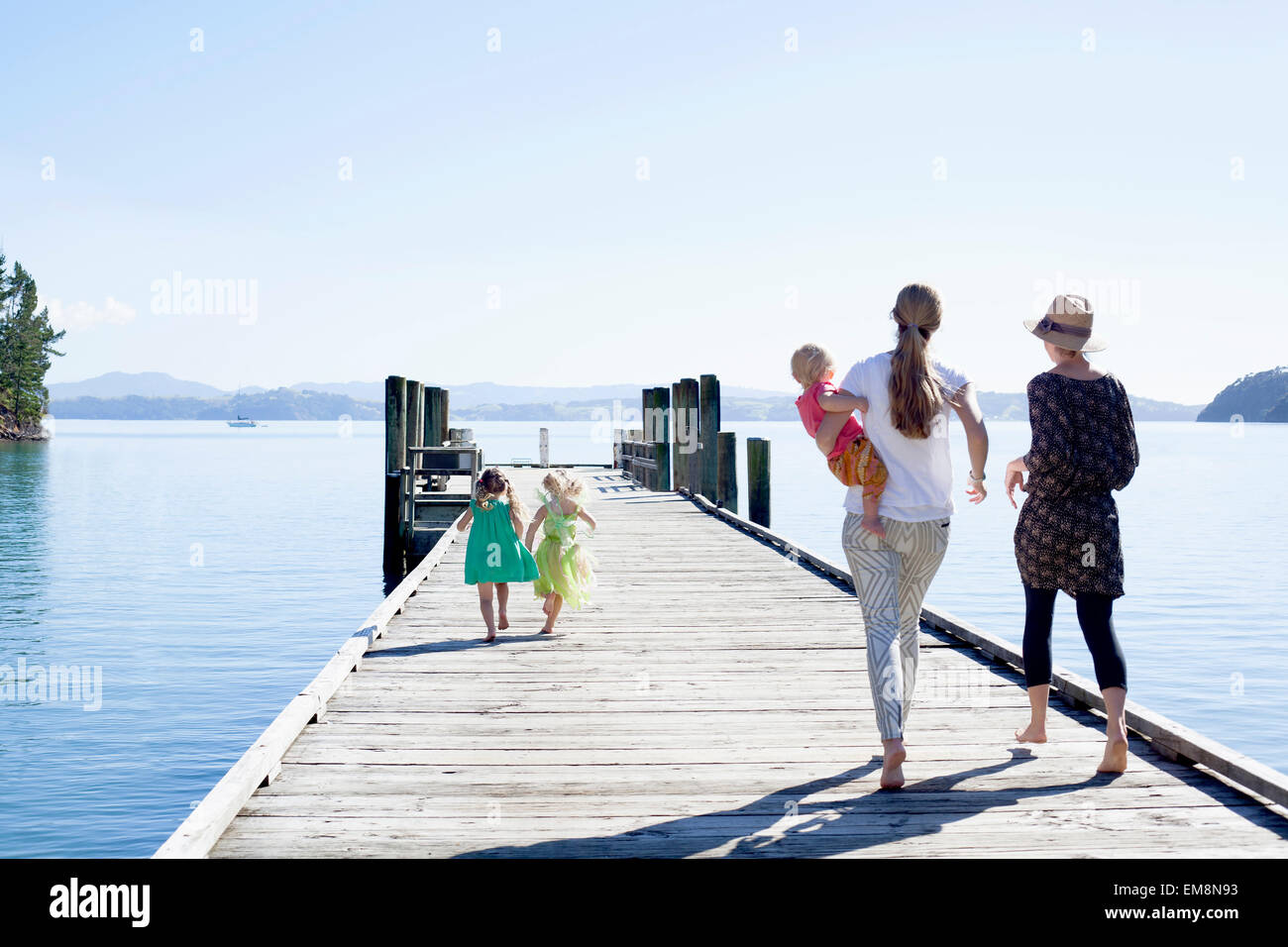 Two mid adult women and daughters strolling on pier, New Zealand Stock Photo