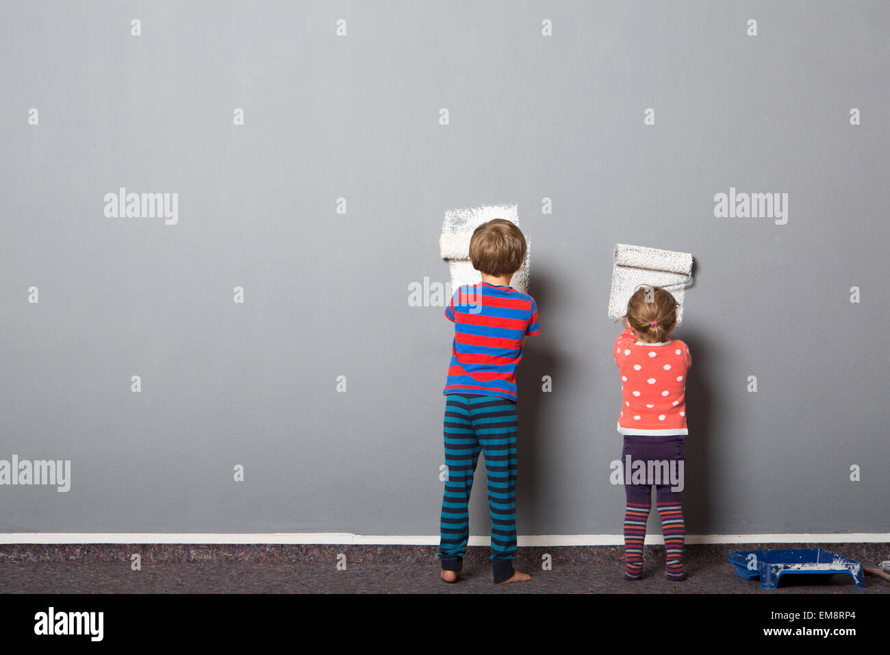 Rear view of brother and toddler sister beginning to paint wall Stock Photo